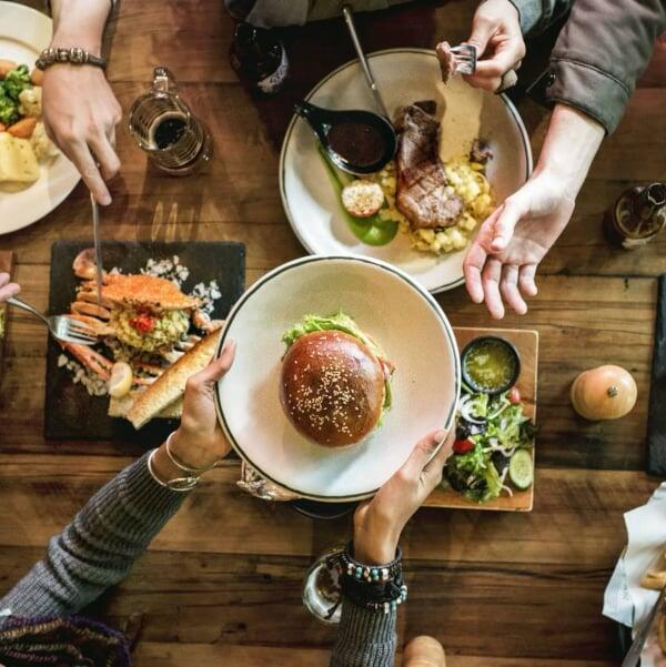 Flera händer som sträcker sig till tallrikar med middagsmat.